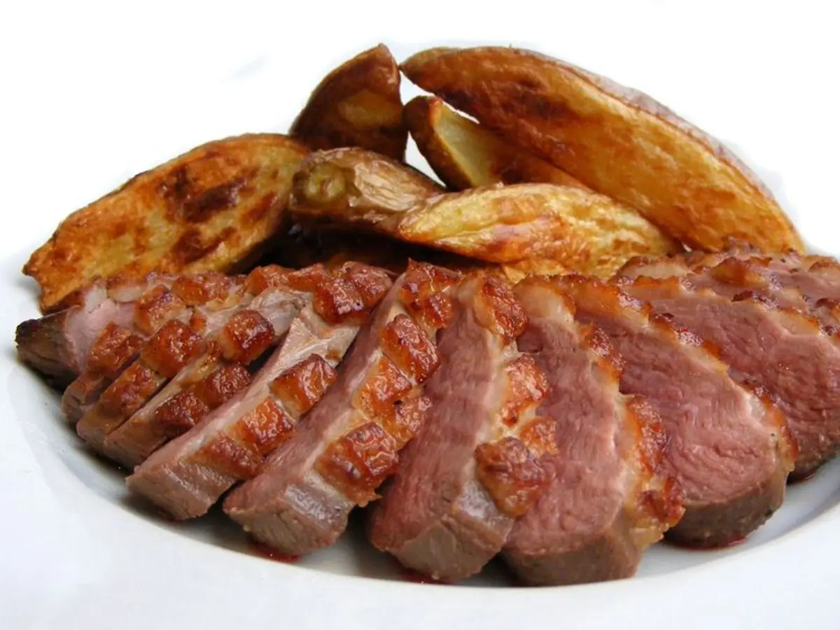 Lonchas de pechuga de pato ahumada y salteada servidas con gajos de patata sobre un plato blanco