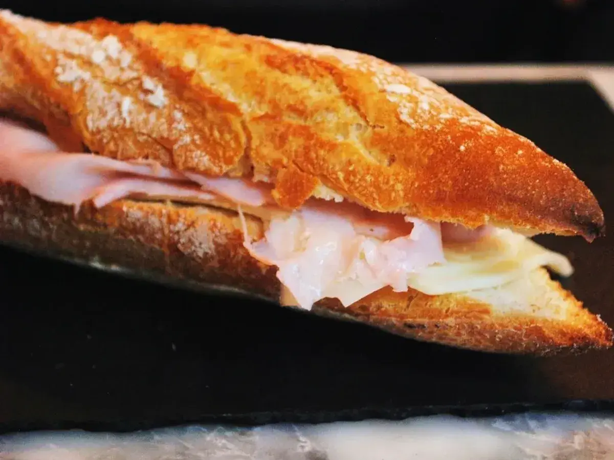 Baguette crujiente abierto relleno de lonchas de jamón y queso sobre fondo oscuro