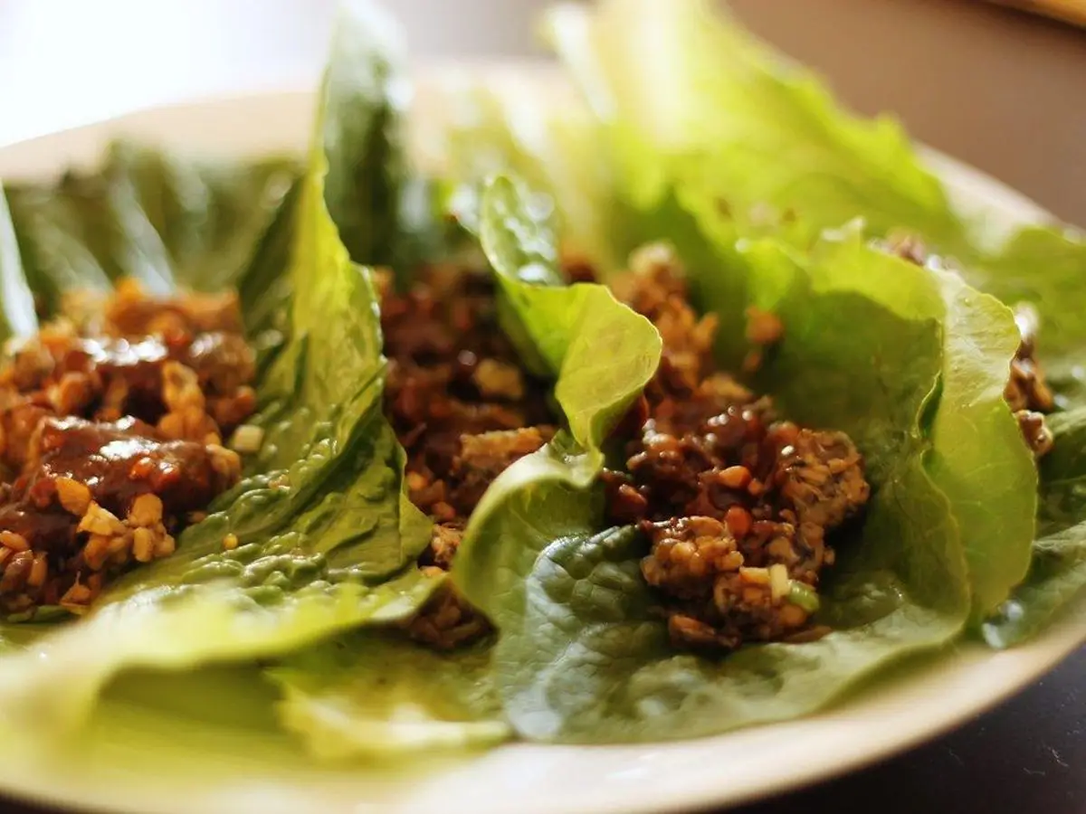 Hojas de lechuga rellenas de carne picada con salsa oscura en un plato blanco