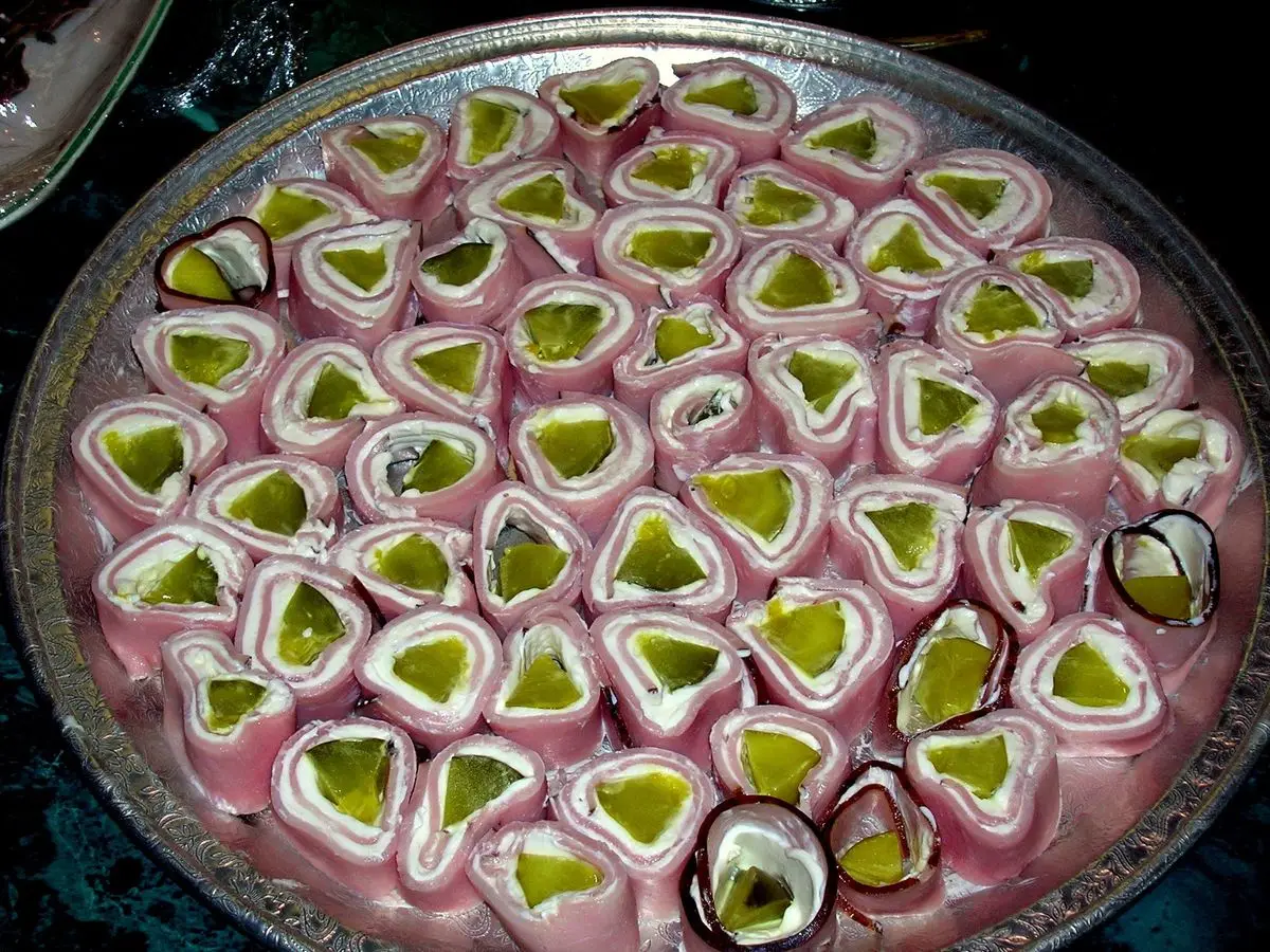 Bandeja de rollitos de jamón rellenos de pepinillo cortados en rodajas y dispuestos en círculo