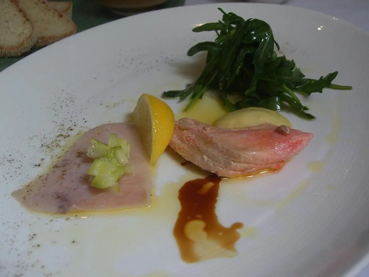 Lonchas finas de pescado con limón y hierbas sobre un plato blanco