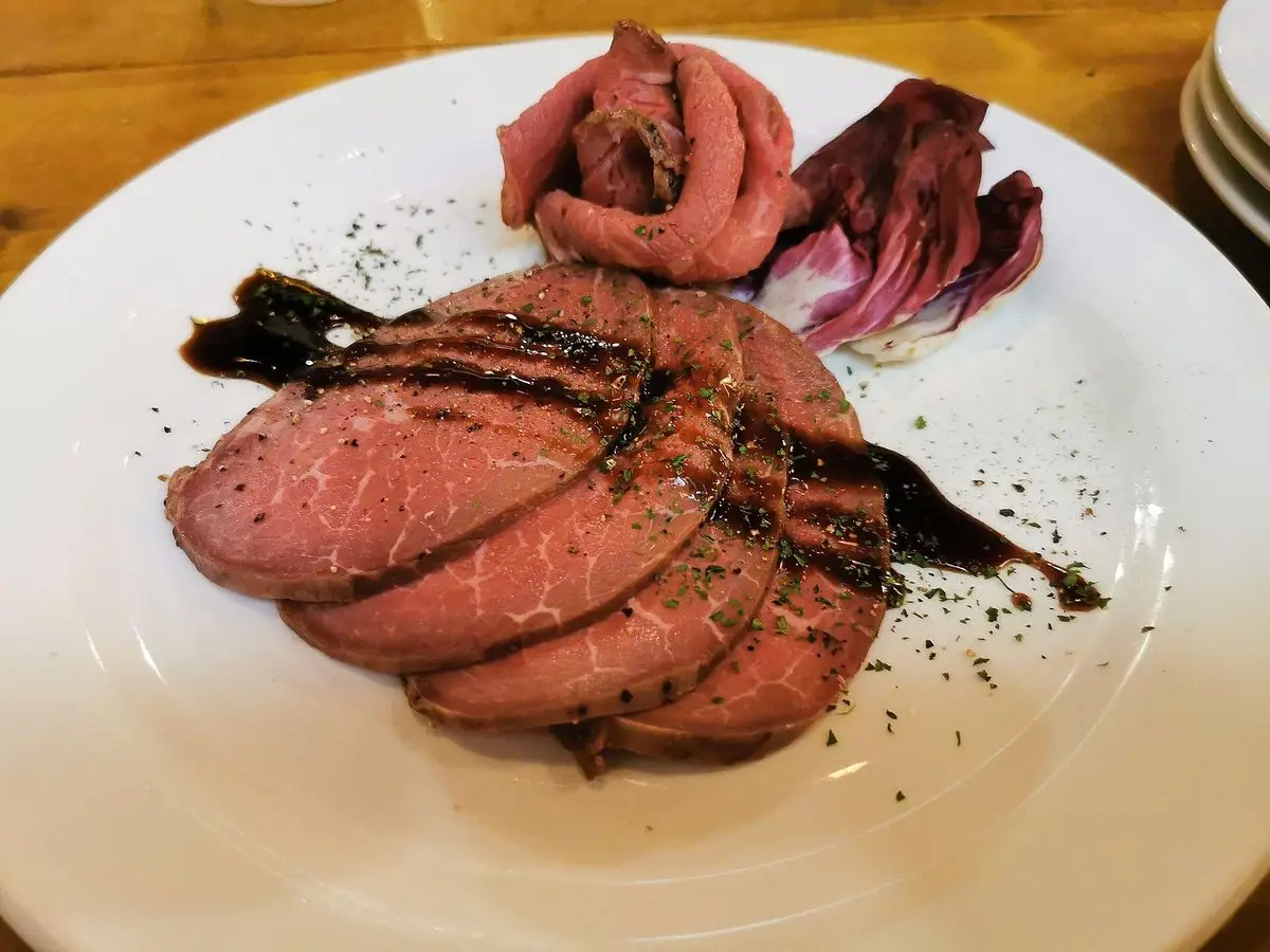 Lonchas de rosbif poco hecho enrolladas en un plato blanco con una guarnición morada