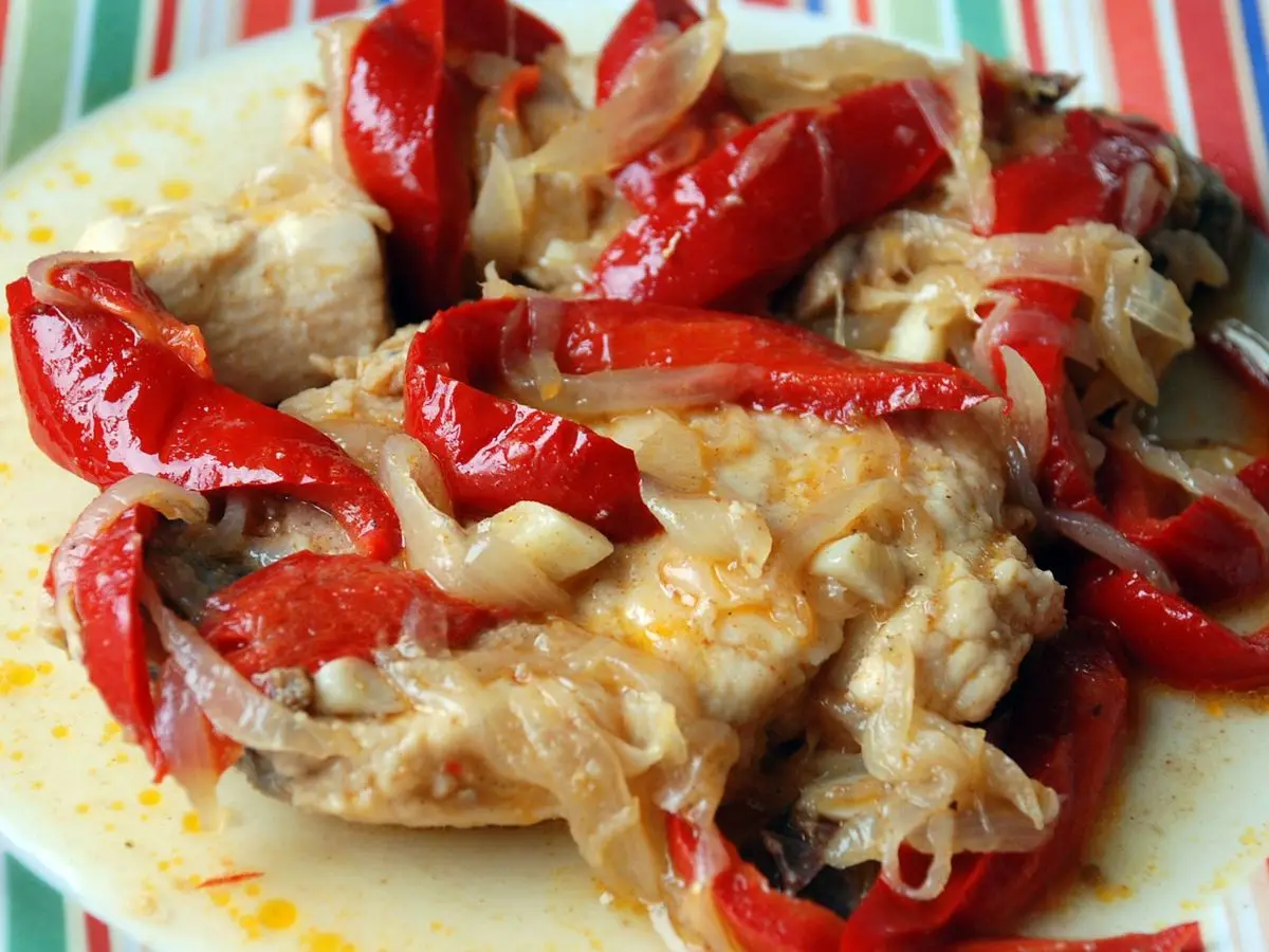 Bonito guisado con tiras de pimiento rojo asado y cebolla en un plato blanco con borde de rayas