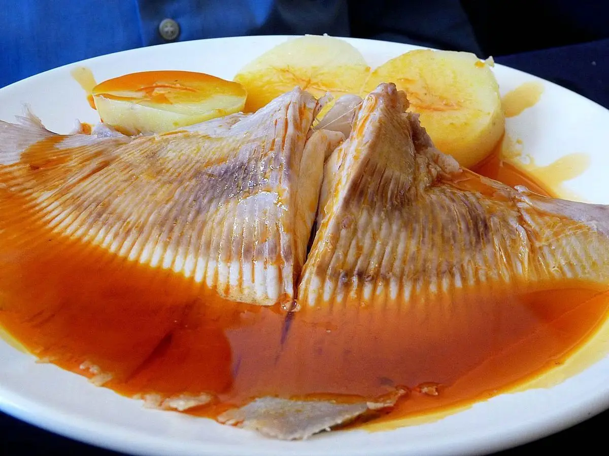 Pescado guisado en salsa roja de pimentón con patatas cocidas en un plato blanco