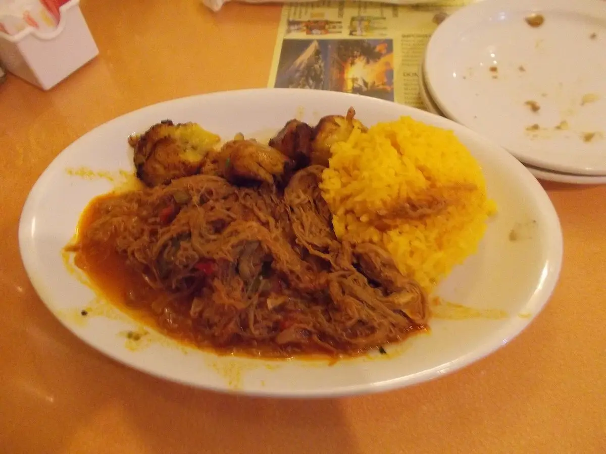 Plato con carne deshilachada en salsa acompañada de arroz amarillo y plátano