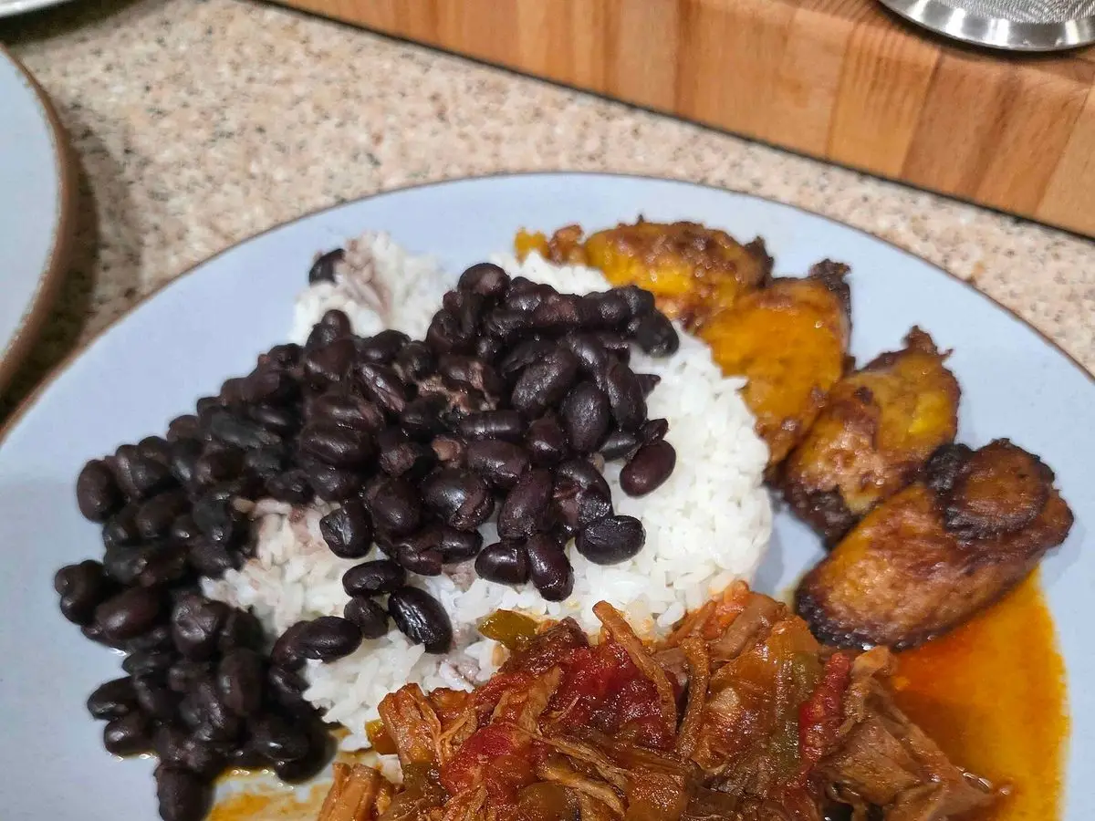 Ternera deshebrada en salsa de tomate con arroz blanco, frijoles negros y plátano frito