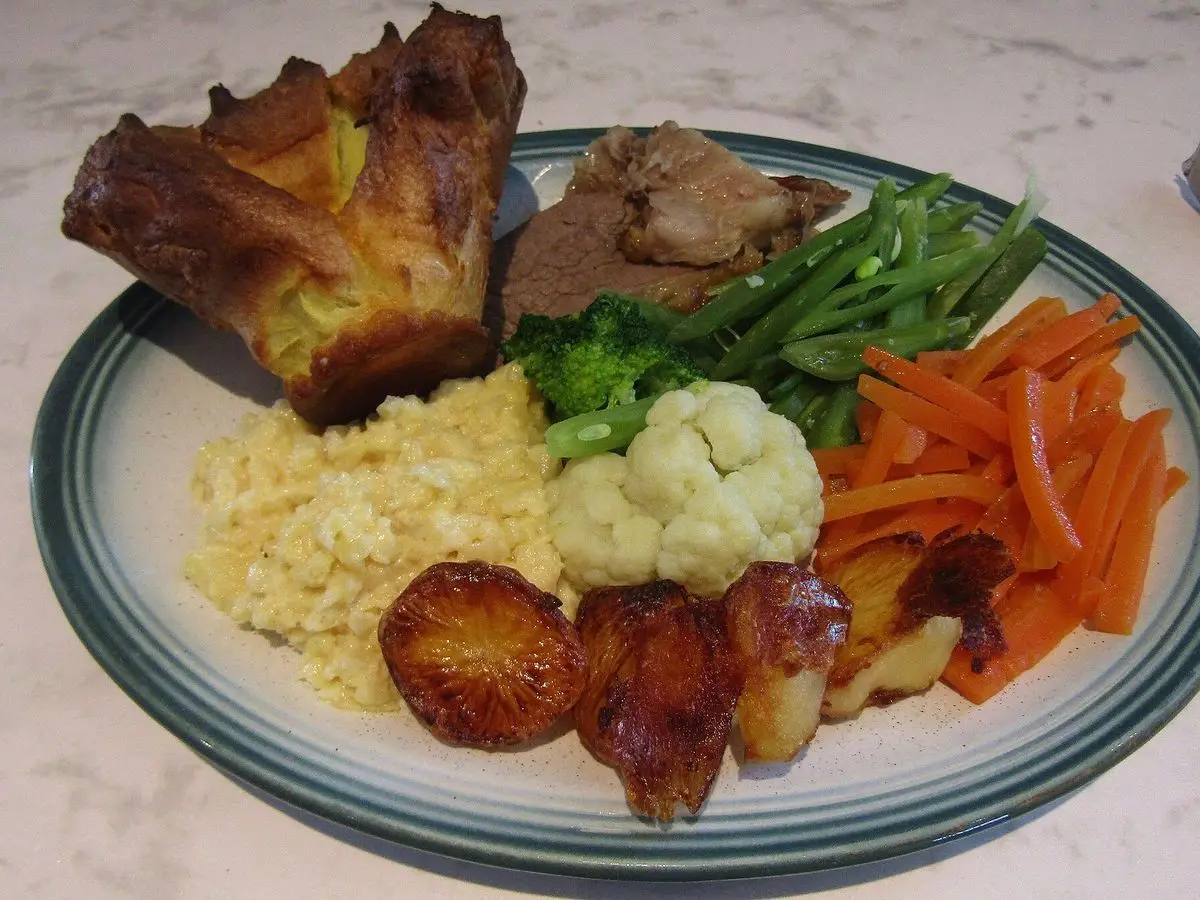 Rosbif con Yorkshire pudding, zanahoria, coliflor, judías verdes y patatas asadas en un plato