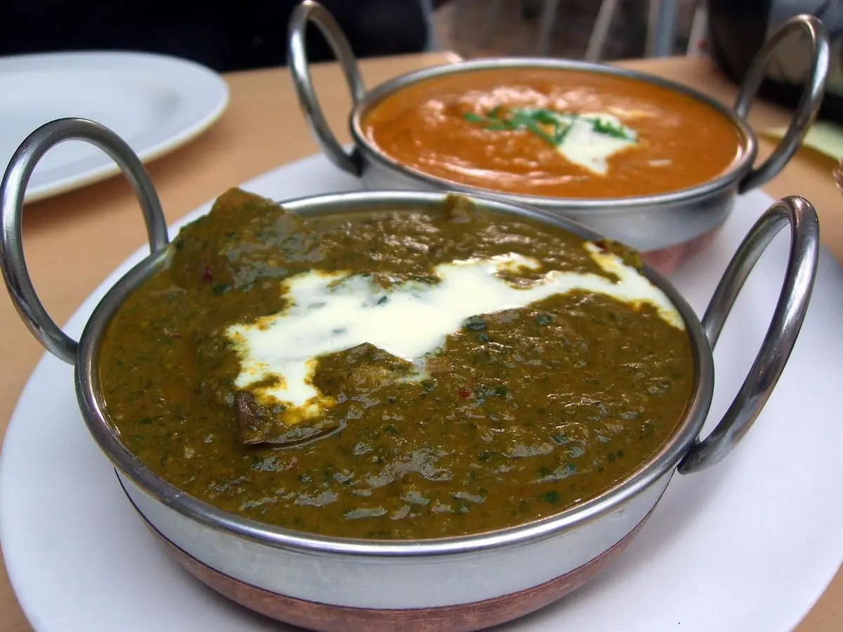 Cuenco metálico de curry verde oscuro de espinacas con cordero y un hilo de nata sobre una mesa