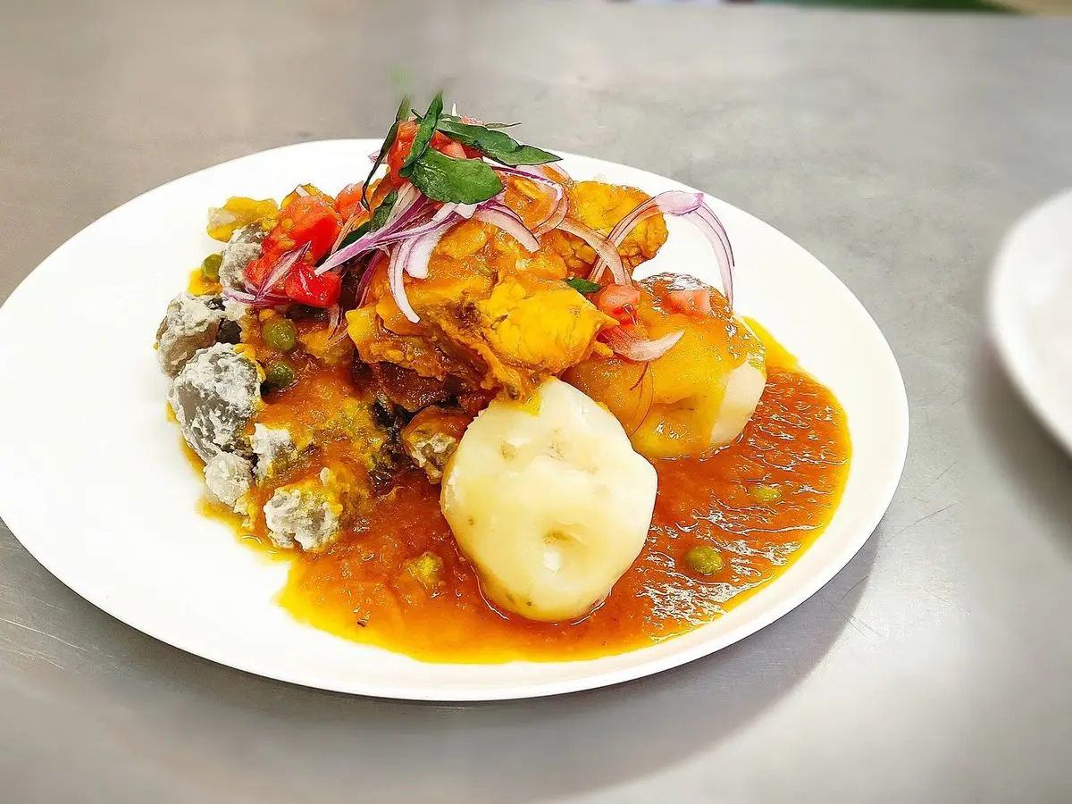 Plato blanco con pollo en salsa de ají anaranjada, patatas y cebolla morada con tomate por encima