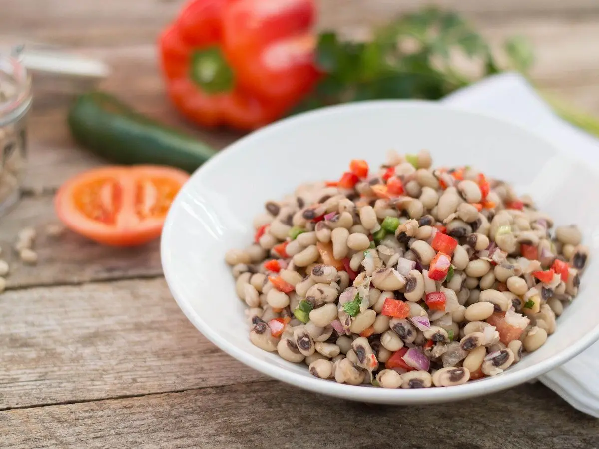 Cuenco blanco de ensalada de judías carillas con tomate y pimiento rojo sobre mesa de madera