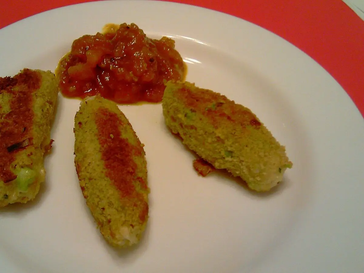 Tres salchichas vegetarianas de queso y puerro doradas con chutney de tomate en un plato blanco