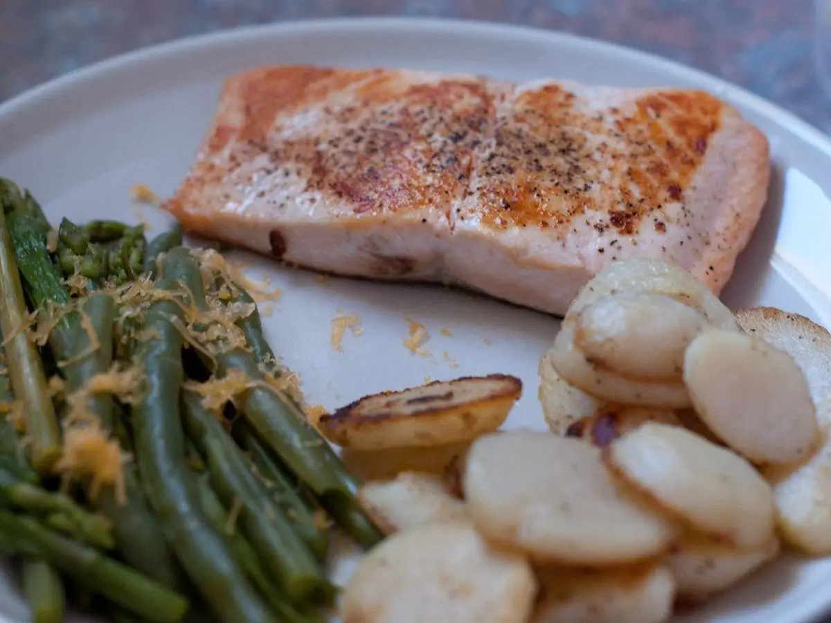 Lomo de salmón asado junto a judías verdes salteadas y rodajas de patata en un plato blanco