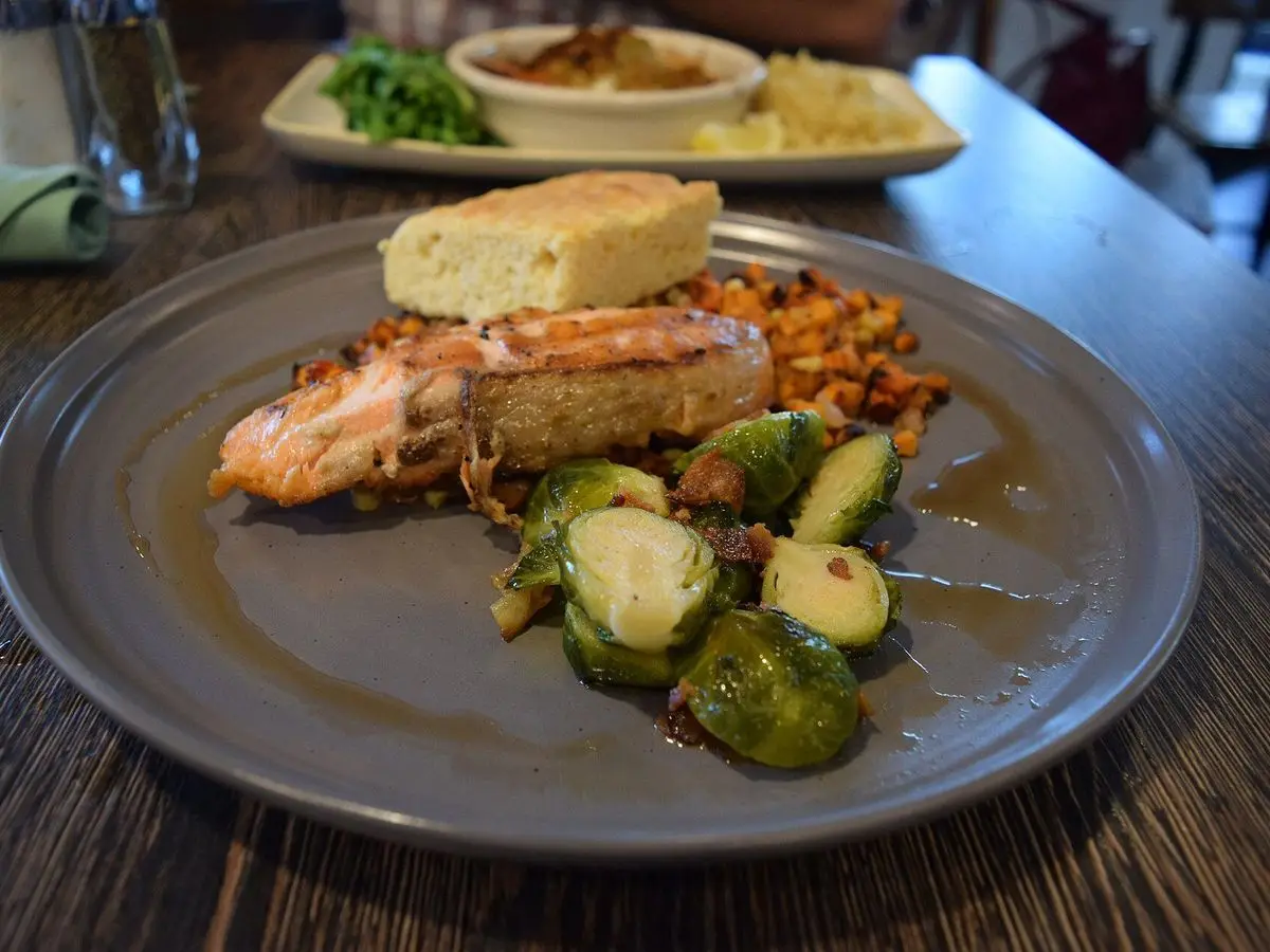 Salmón glaseado con boniato salteado y coles de Bruselas en un plato gris sobre mesa oscura