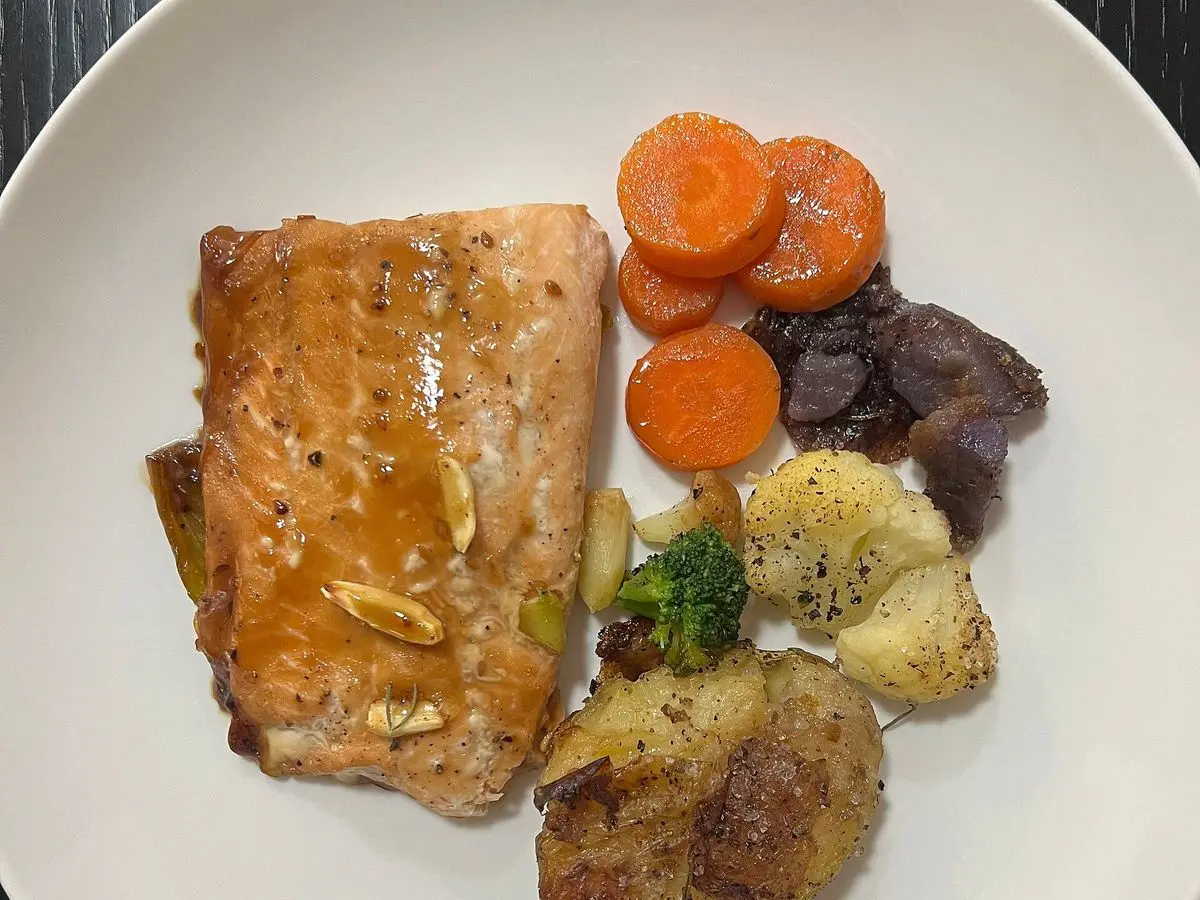 Filete de salmón dorado con patatas asadas, zanahoria y brócoli en un plato blanco