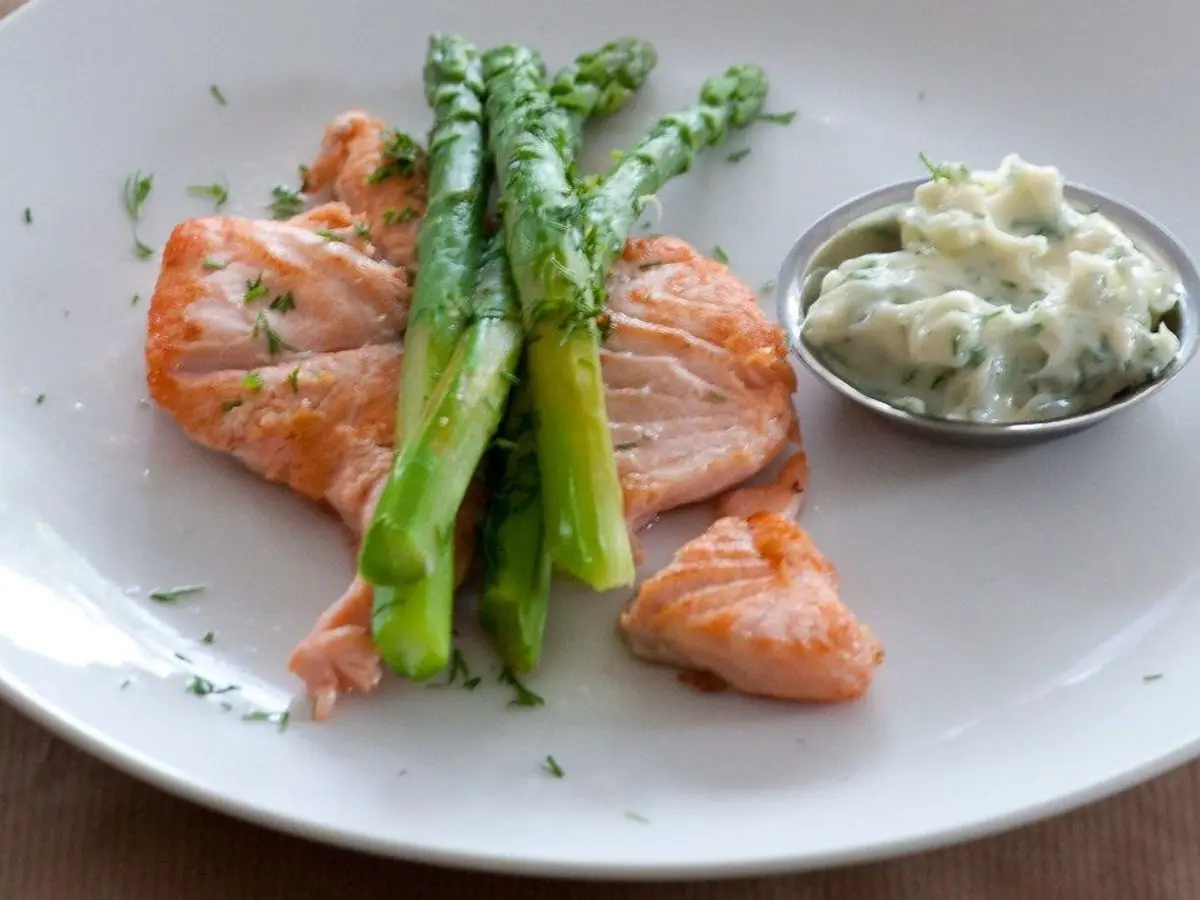 Trozos de salmón con espárragos verdes y eneldo, junto a un cuenquito de salsa blanca con hierbas