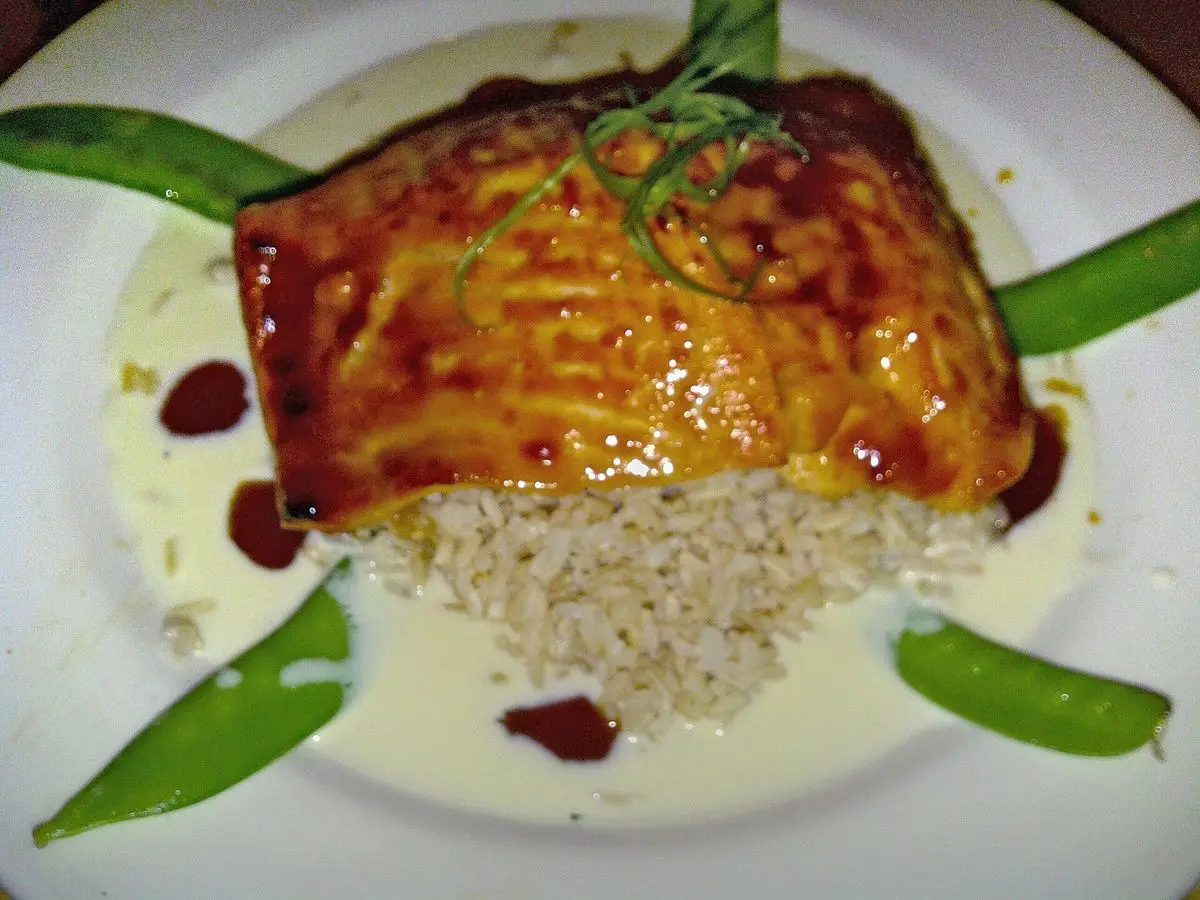 Filete de salmón glaseado y brillante sobre un lecho de arroz con vainas verdes a los lados