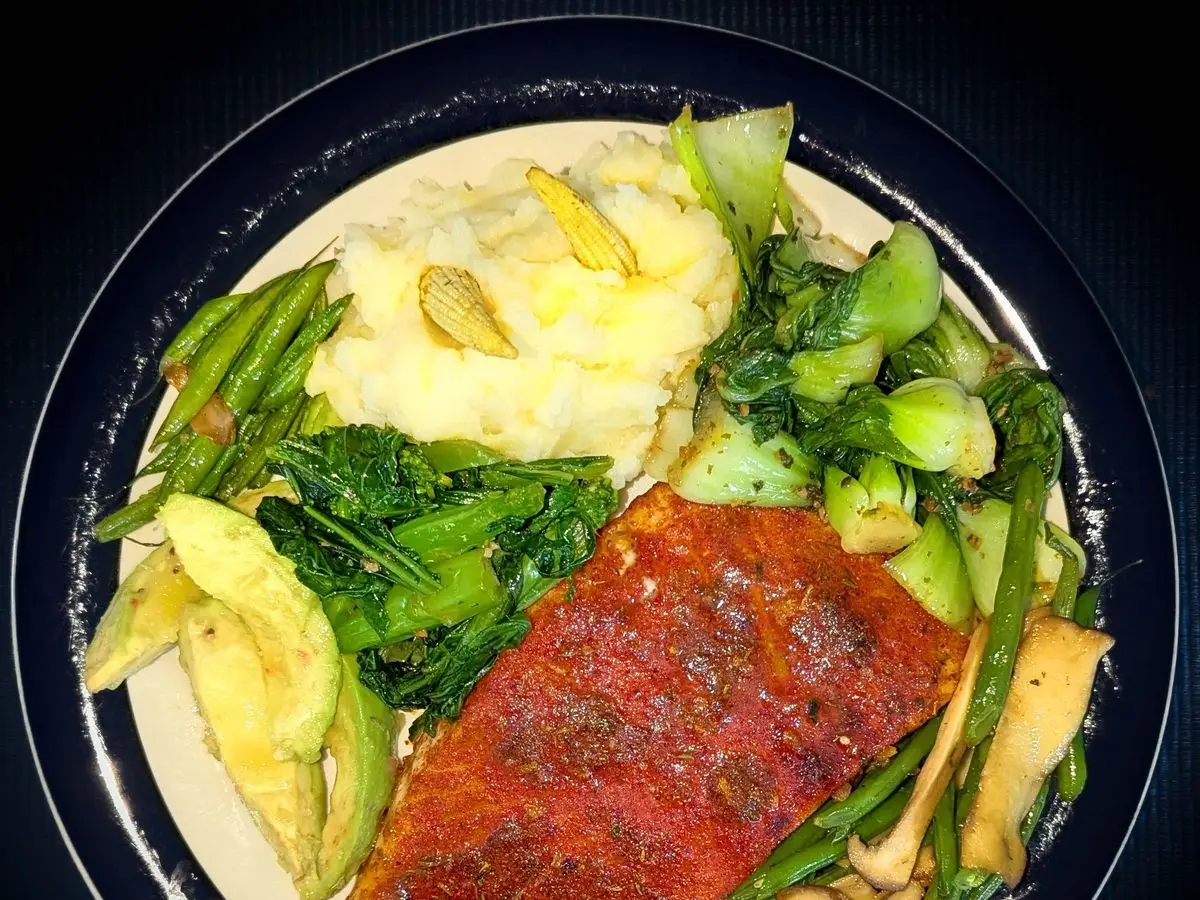 Salmón al horno con puré cremoso, verduras de hoja verde, judías verdes y aguacate en un plato oscuro
