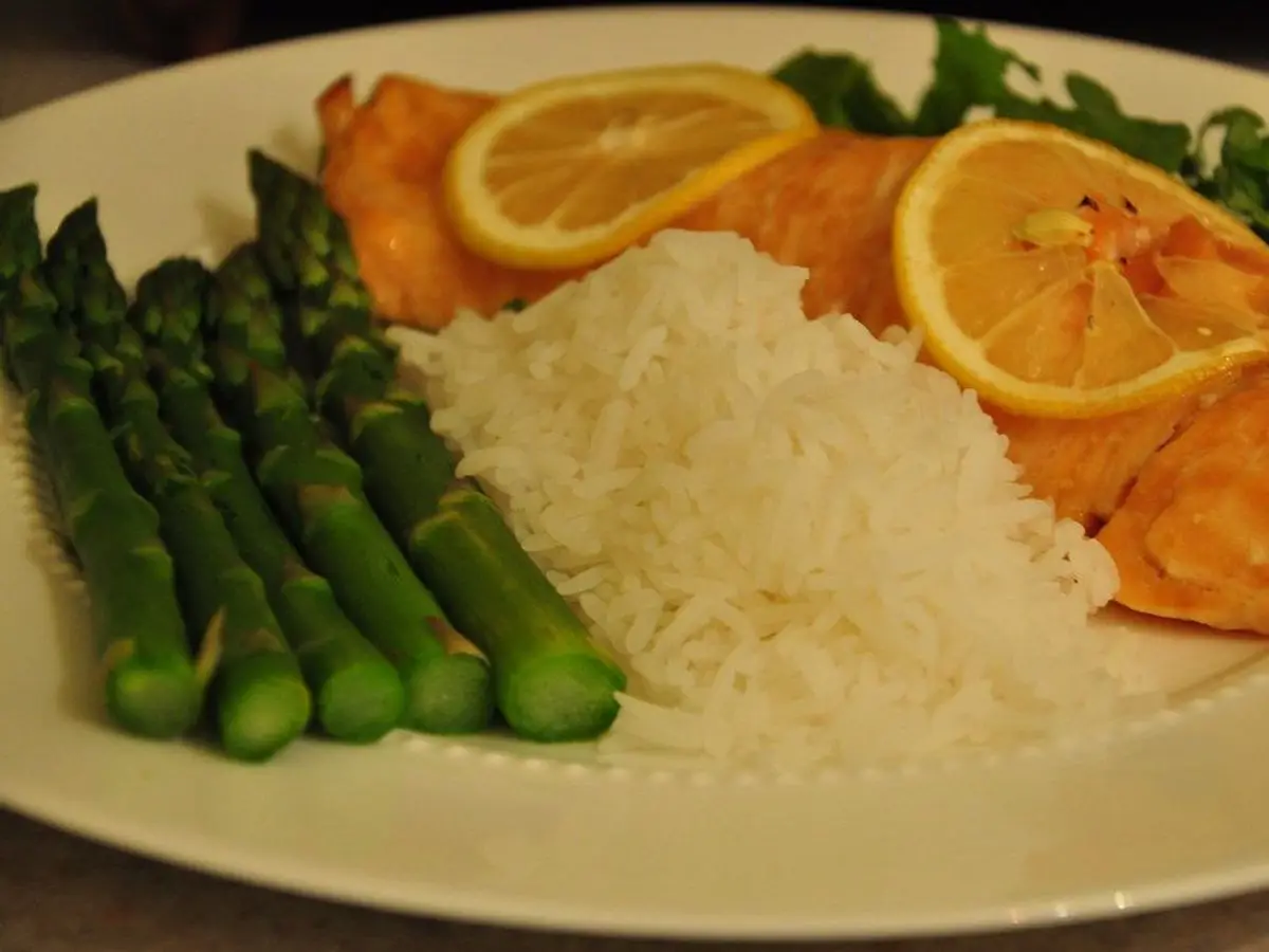 Filete de salmón con rodajas de naranja, arroz blanco y espárragos verdes en un plato