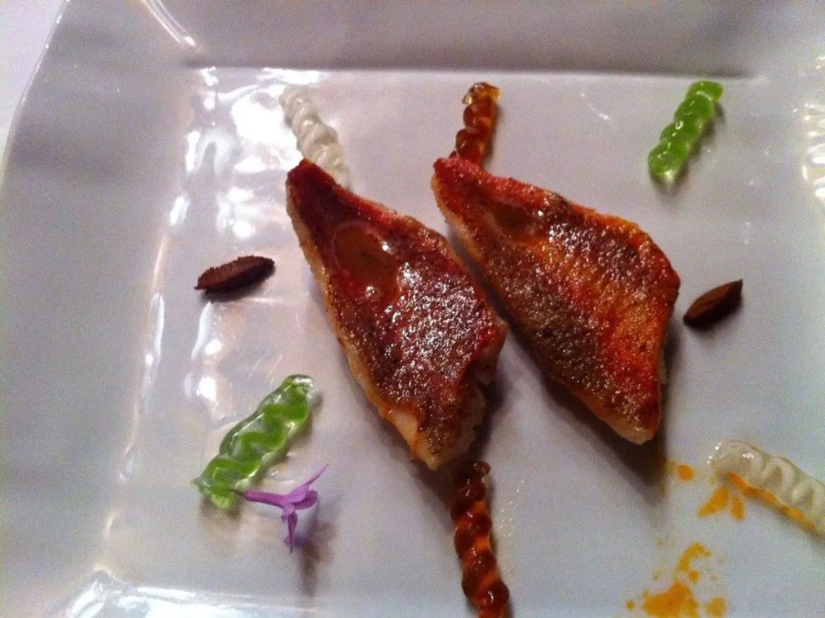 Dos filetes de salmonete dorados con la piel rojiza en un plato cuadrado blanco con pequeños adornos