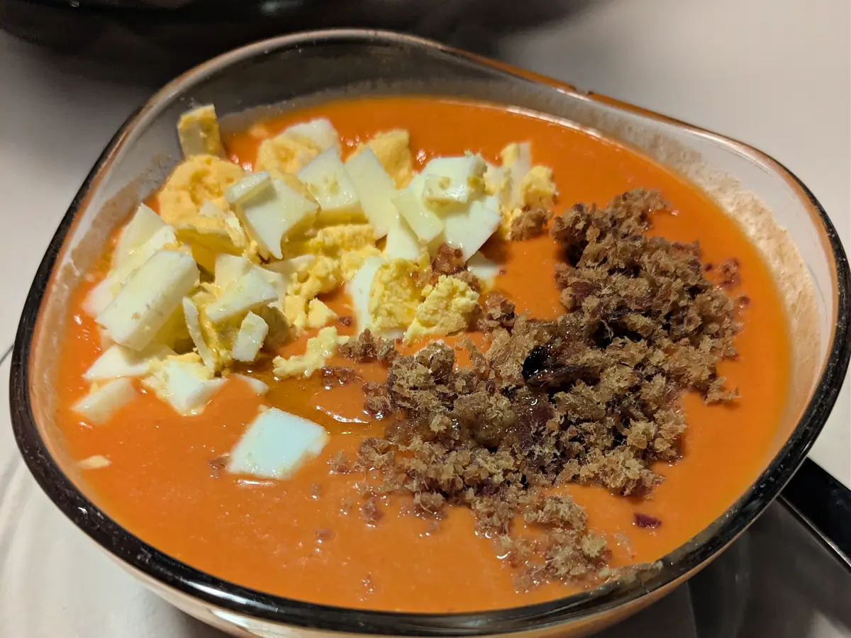 Cuenco de salmorejo anaranjado con huevo duro picado y migas oscuras por encima