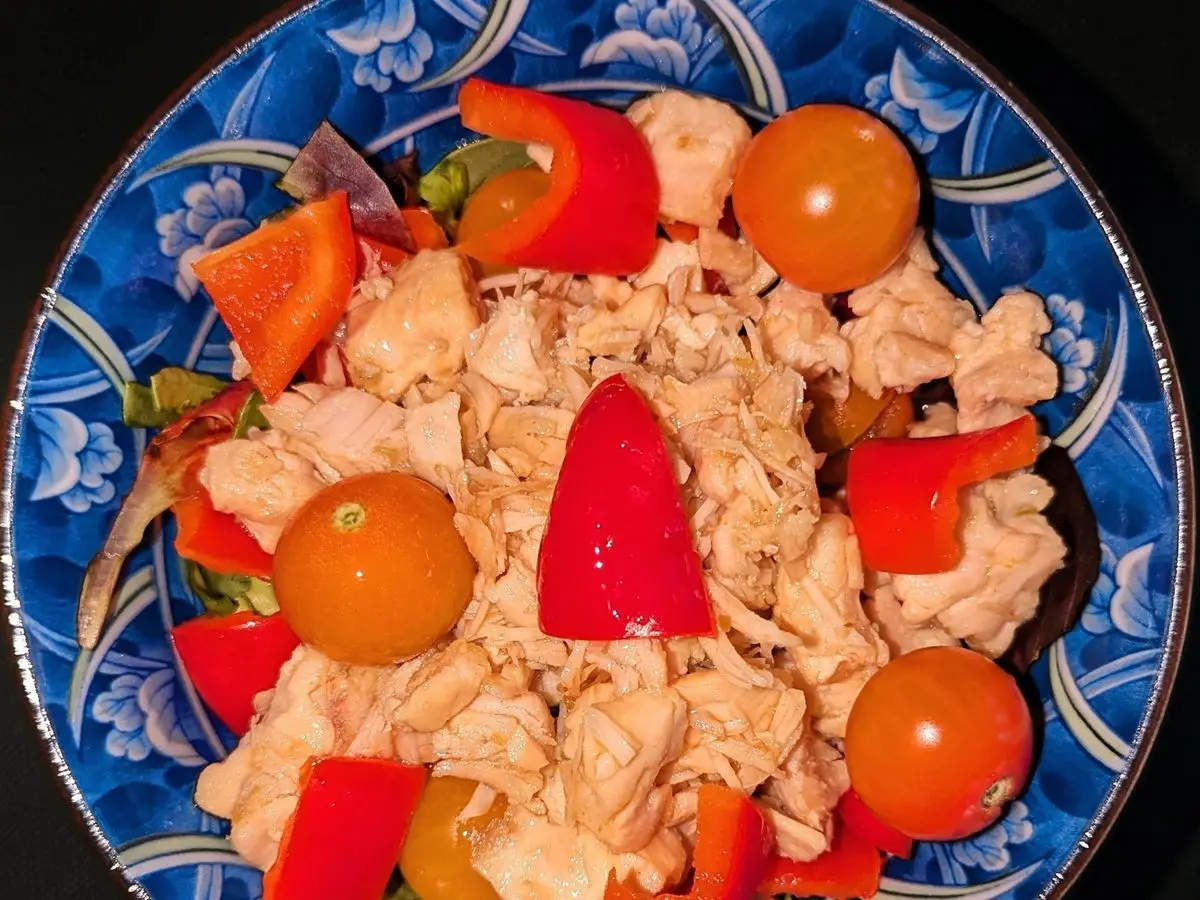 Plato azul con ensalada de pollo desmenuzado, pimiento rojo, tomates cherry y cebolla