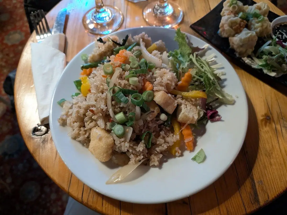 Plato blanco de arroz salteado con tofu, zanahoria y verduras sobre una mesa de madera