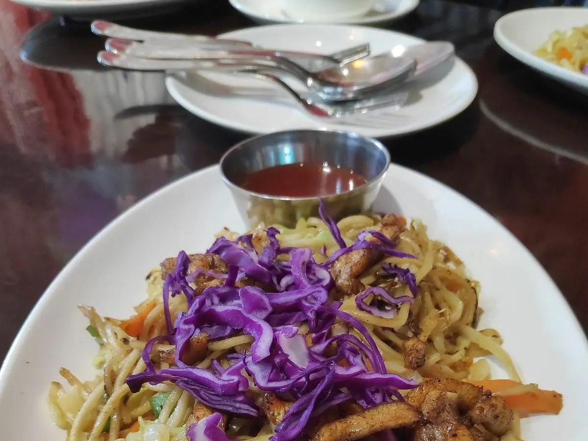 Plato blanco con fideos salteados, tiras de pollo, col morada rallada y verduras