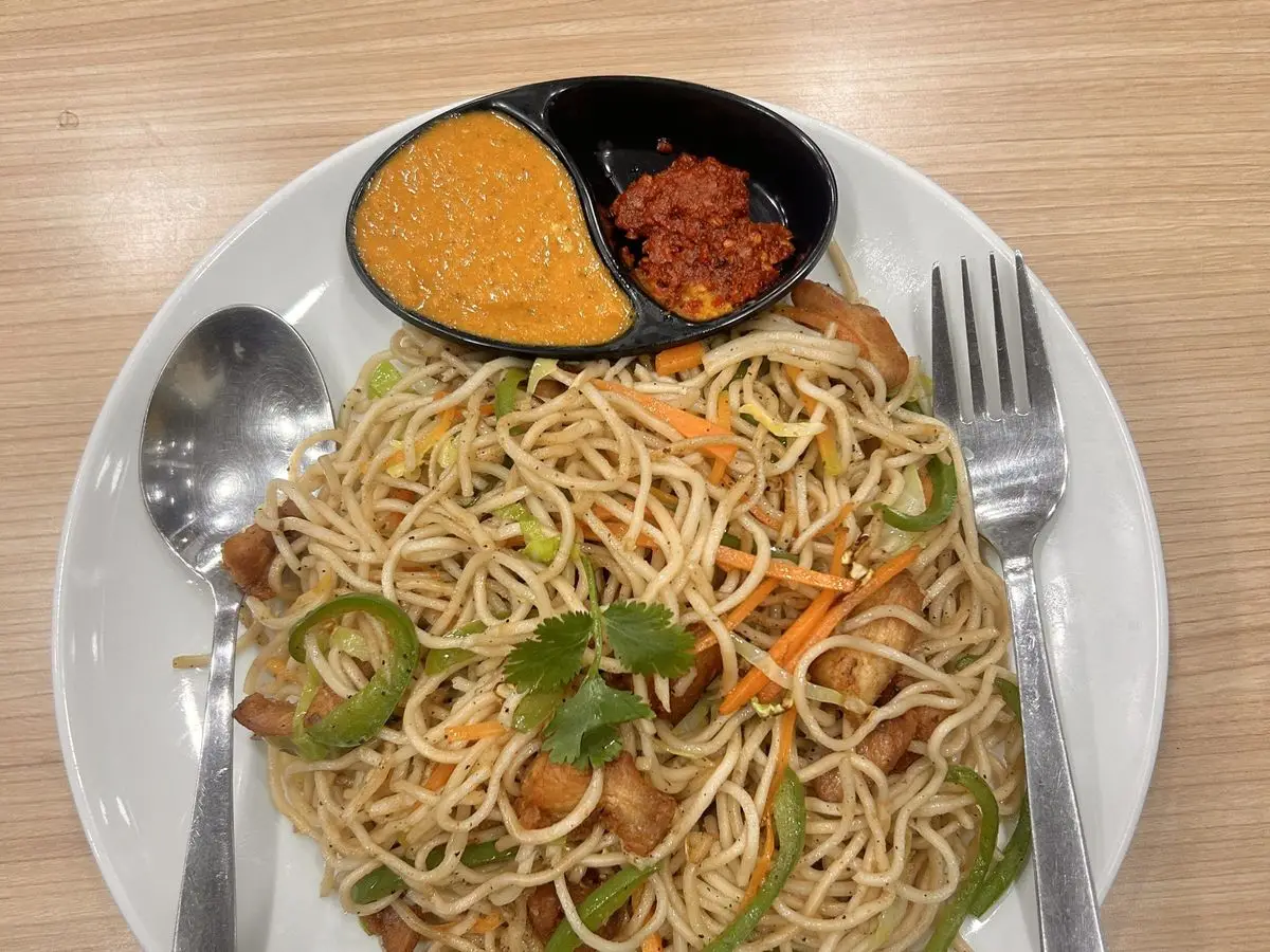 Fideos salteados con pollo, pimiento verde y zanahoria en un plato blanco, con dos salsas al lado