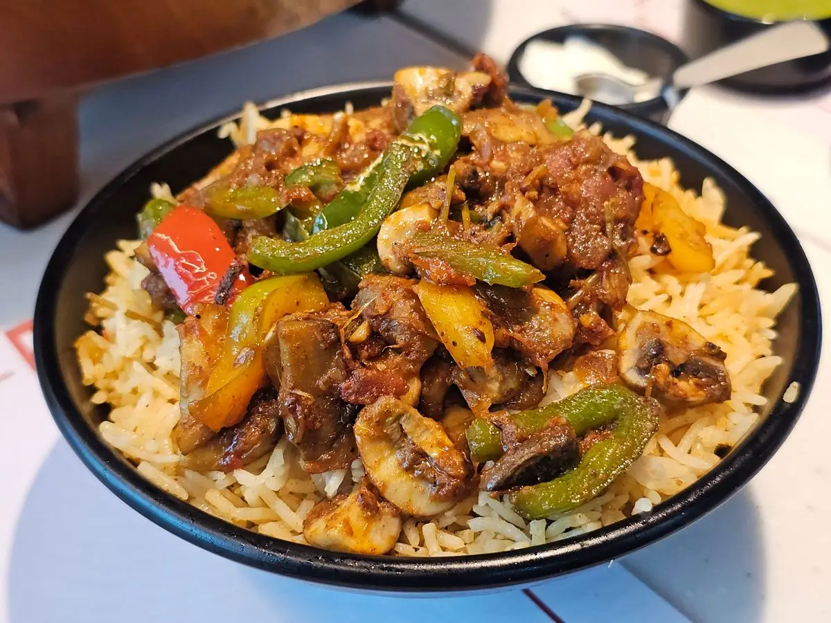 Bol de arroz cubierto con un salteado de champiñones, carne y pimientos verde y rojo en salsa