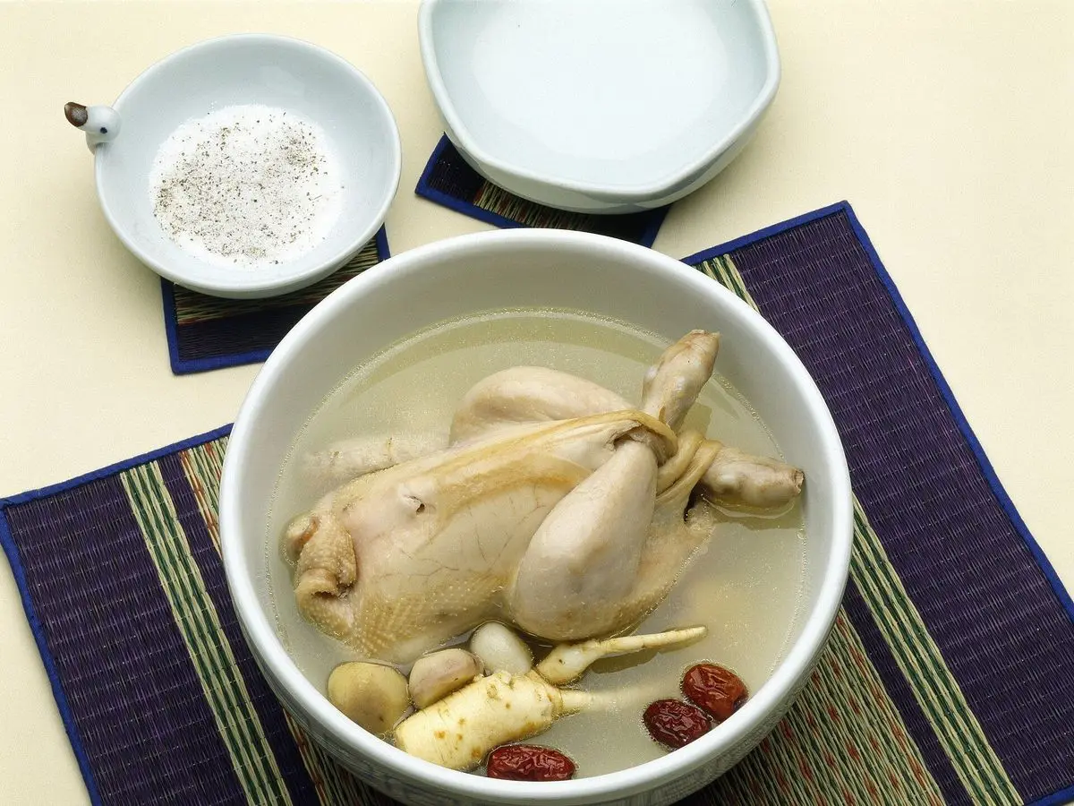 Cuenco de sopa coreana con un pollo entero, ajo, ginseng y dátiles rojos sobre un mantel