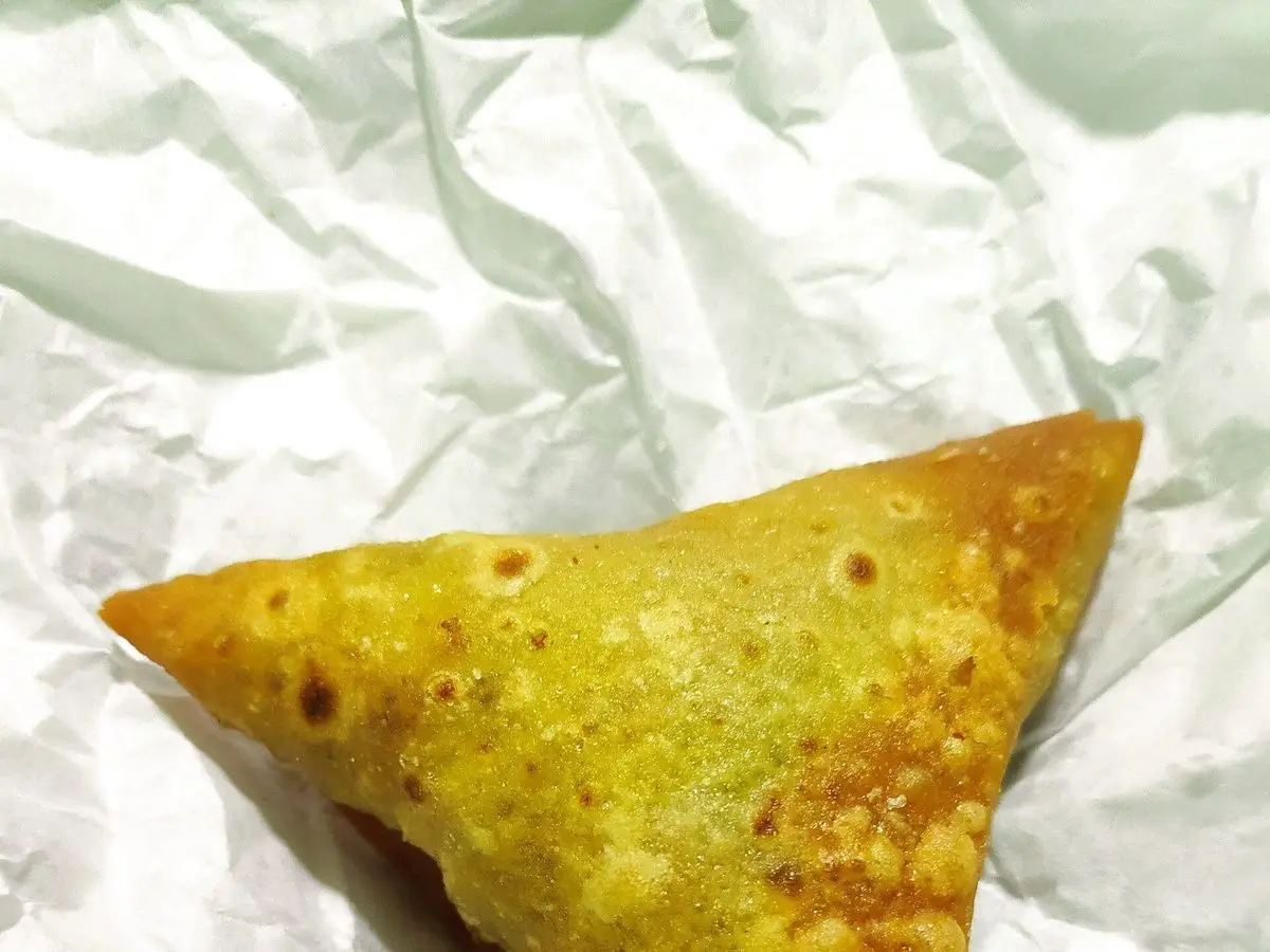 Samosa triangular de masa dorada sobre papel blanco, vista de cerca