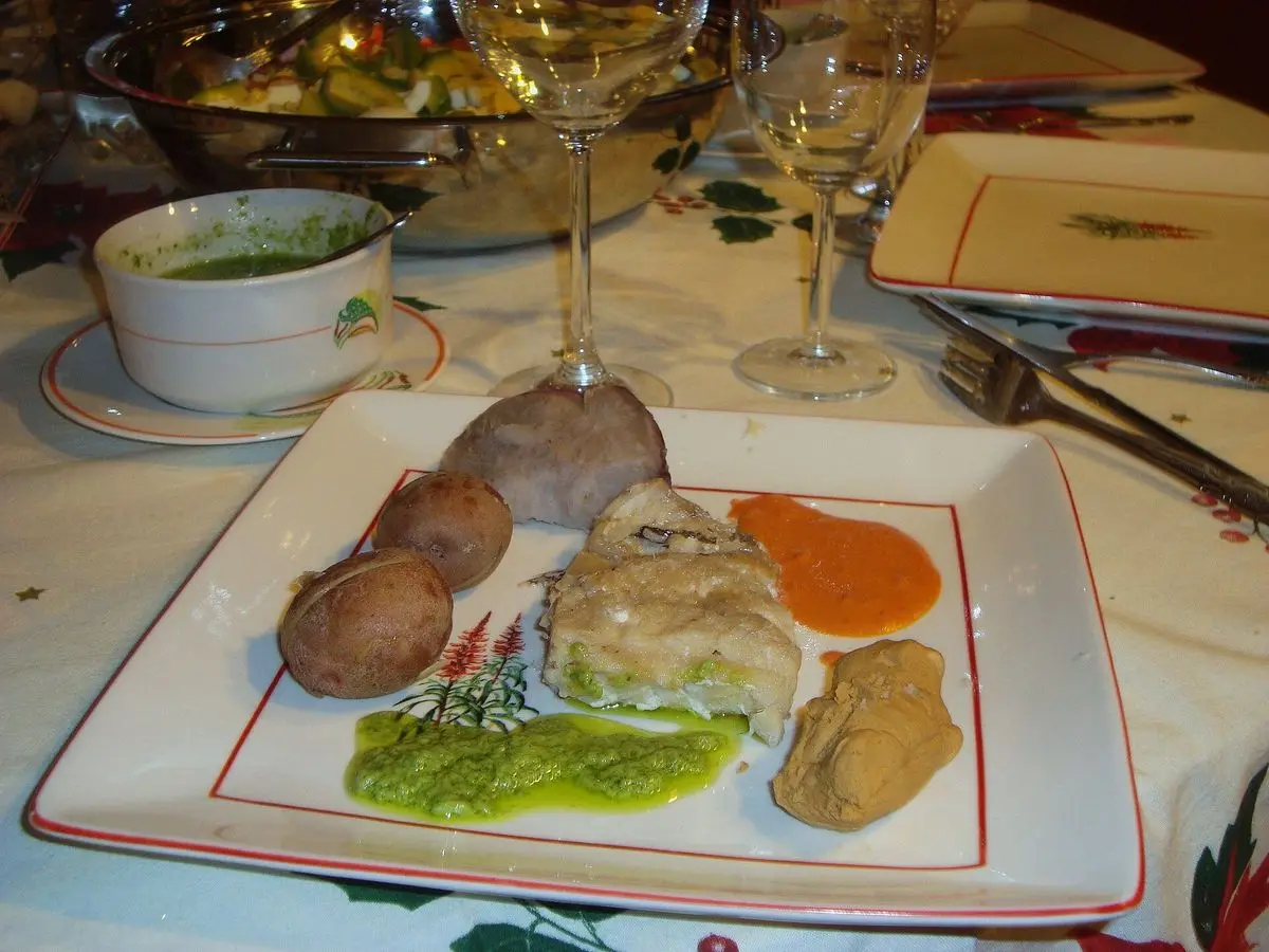 Plato cuadrado con pescado, papas arrugadas, batata y mojo verde en una taza sobre una mesa puesta