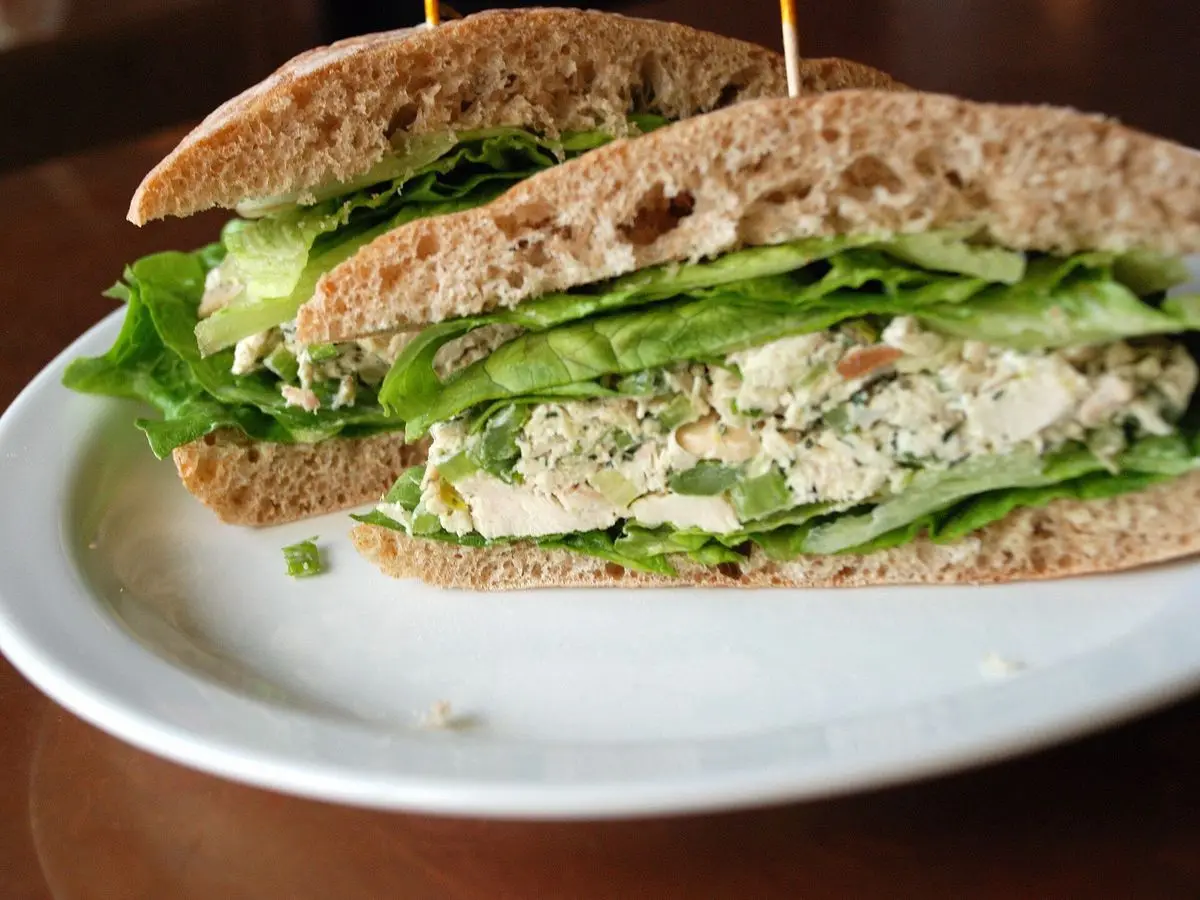 Sándwich de pan integral con ensalada de pollo y hojas de lechuga sobre un plato blanco