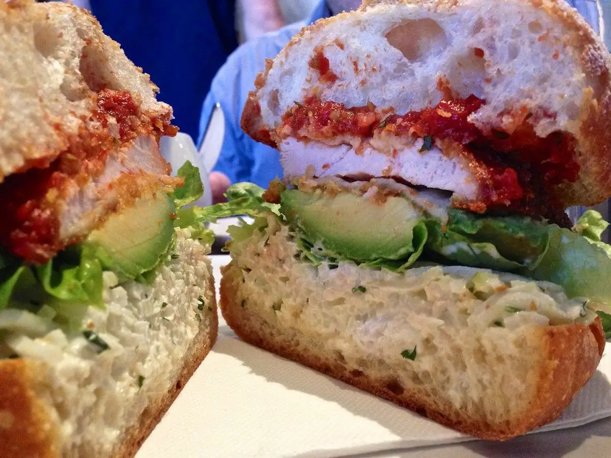 Sándwich abierto de pollo empanado con aguacate, lechuga y salsa en pan rústico