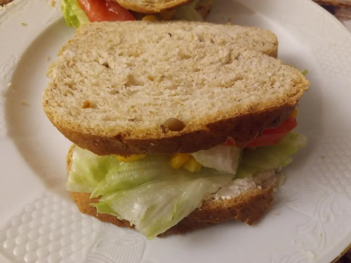 Sándwich de pan integral con lechuga, tomate y crema de tofu en un plato blanco