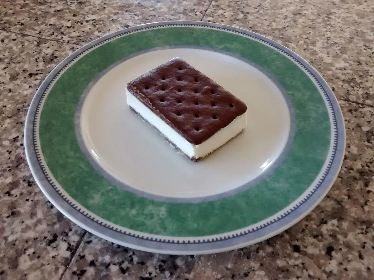 Sándwich helado rectangular de galleta oscura y relleno blanco sobre un plato con borde verde