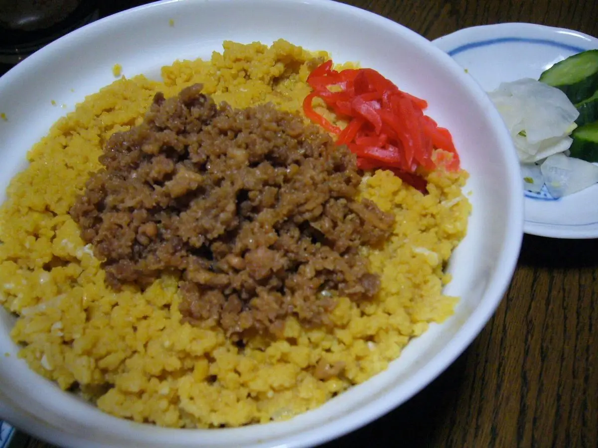 Cuenco de arroz con huevo revuelto amarillo, picadillo de carne y tomate rojo, con ensalada al lado