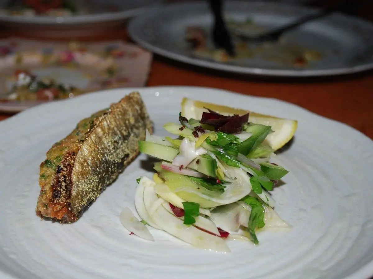 Sardina rellena a la plancha con ensalada de hinojo y hierbas sobre un plato blanco