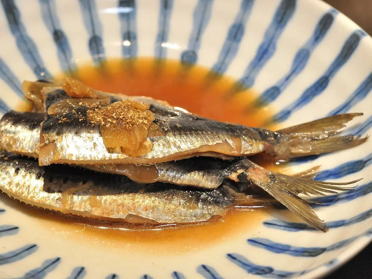 Sardinas guisadas con jengibre en una salsa oscura sobre un plato de cerámica azul y blanco