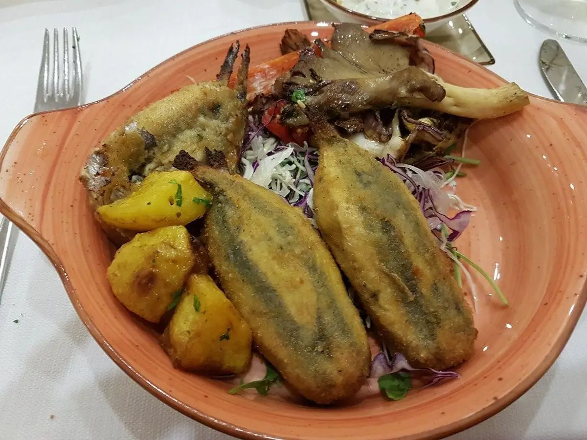 Cazuela de barro ovalada con sardinas rellenas doradas, patatas y ensalada