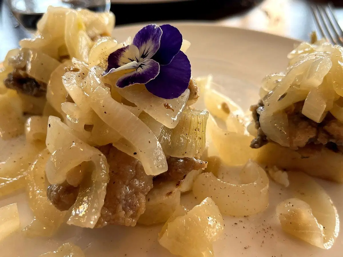 Sardinas en saor con cebolla cocida y pasas sobre rebanadas de polenta, con una flor violeta