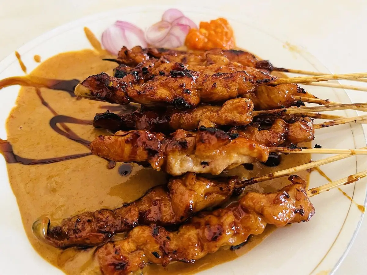 Brochetas de pollo a la parrilla sobre salsa de cacahuete con cebolla morada en un plato blanco