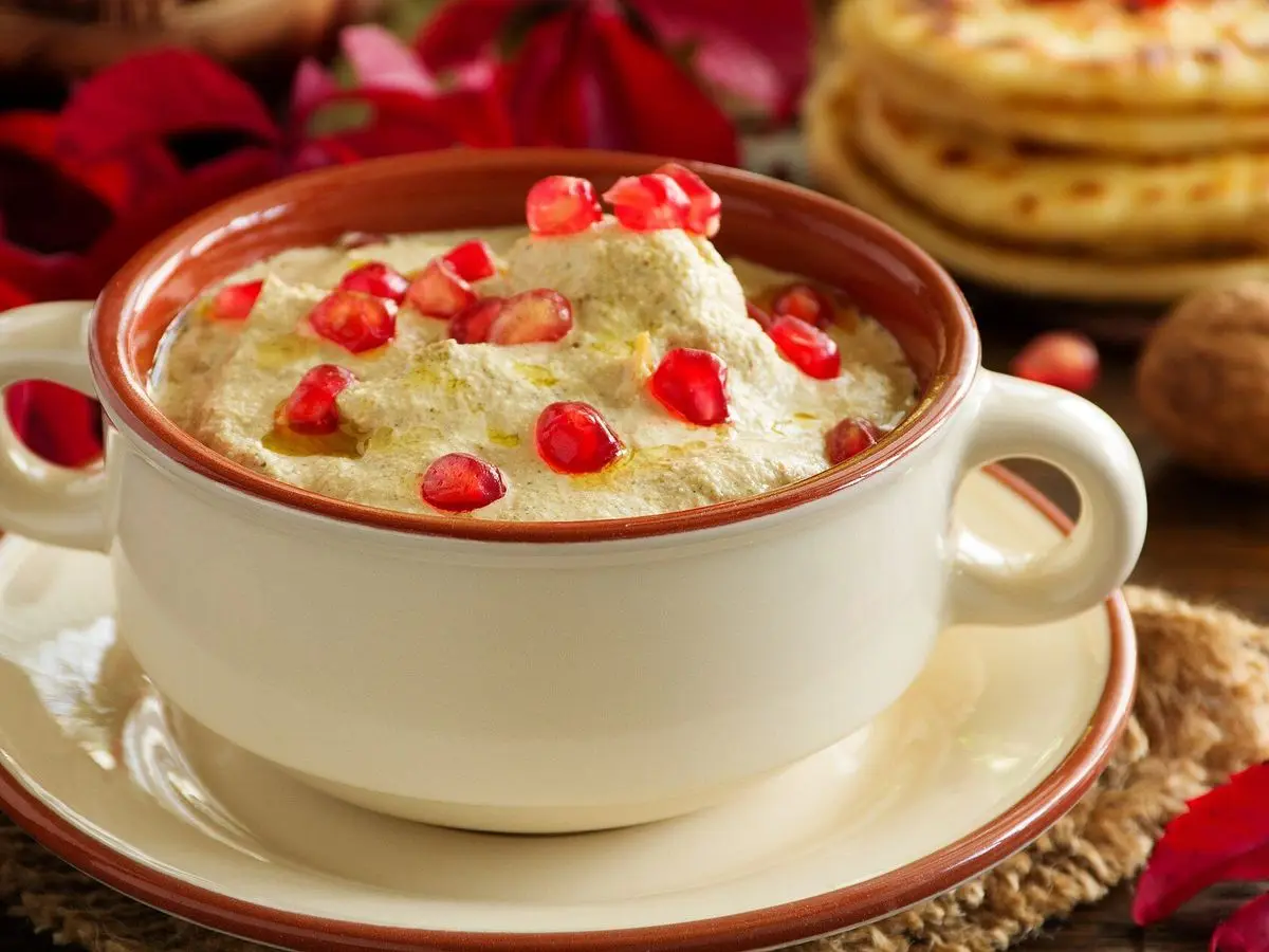 Cuenco de satsivi, carne en salsa cremosa de nueces con granos de granada por encima y panes planos al fondo