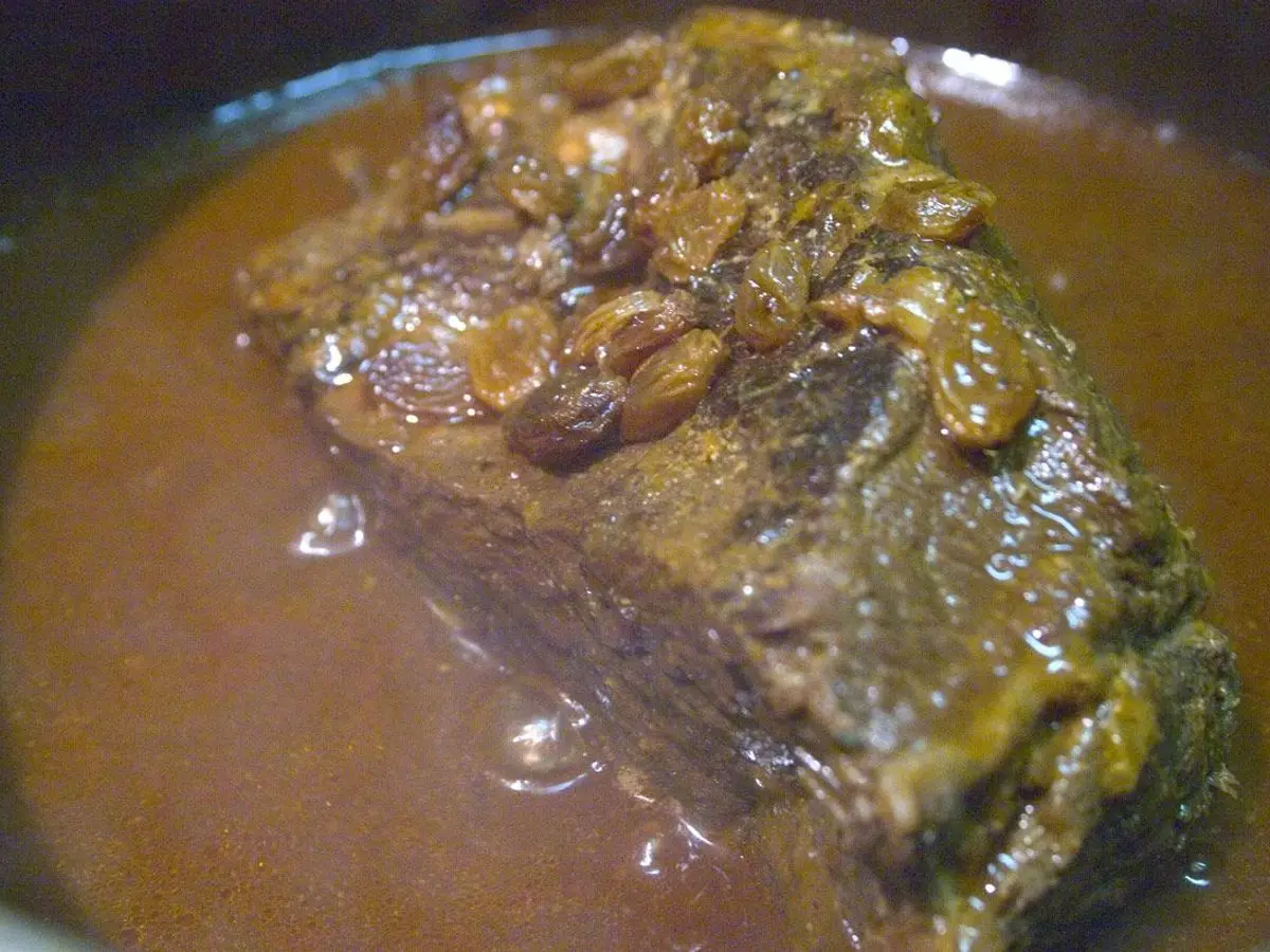 Pieza de carne asada en salsa marrón espesa con pasas por encima en una fuente