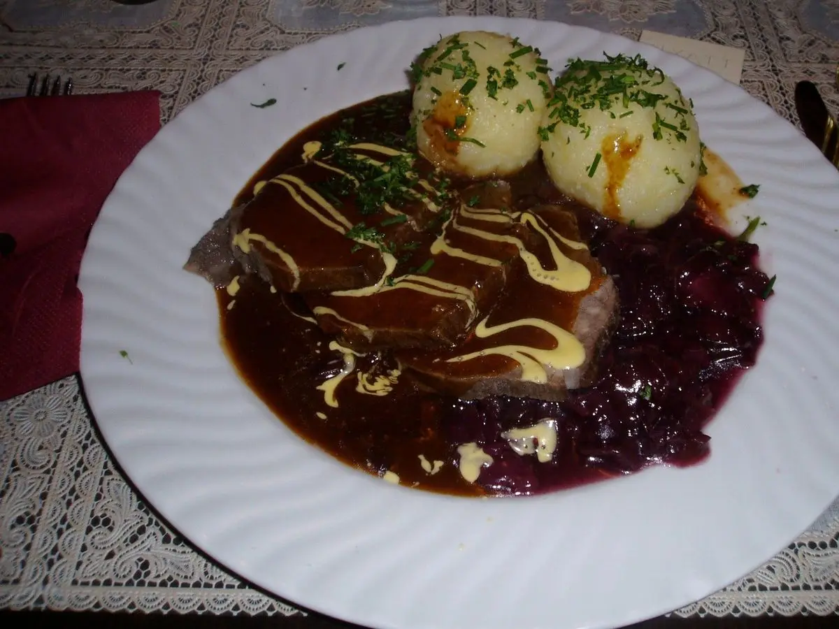 Sauerbraten con salsa oscura, lombarda y bolas de patata en un plato blanco