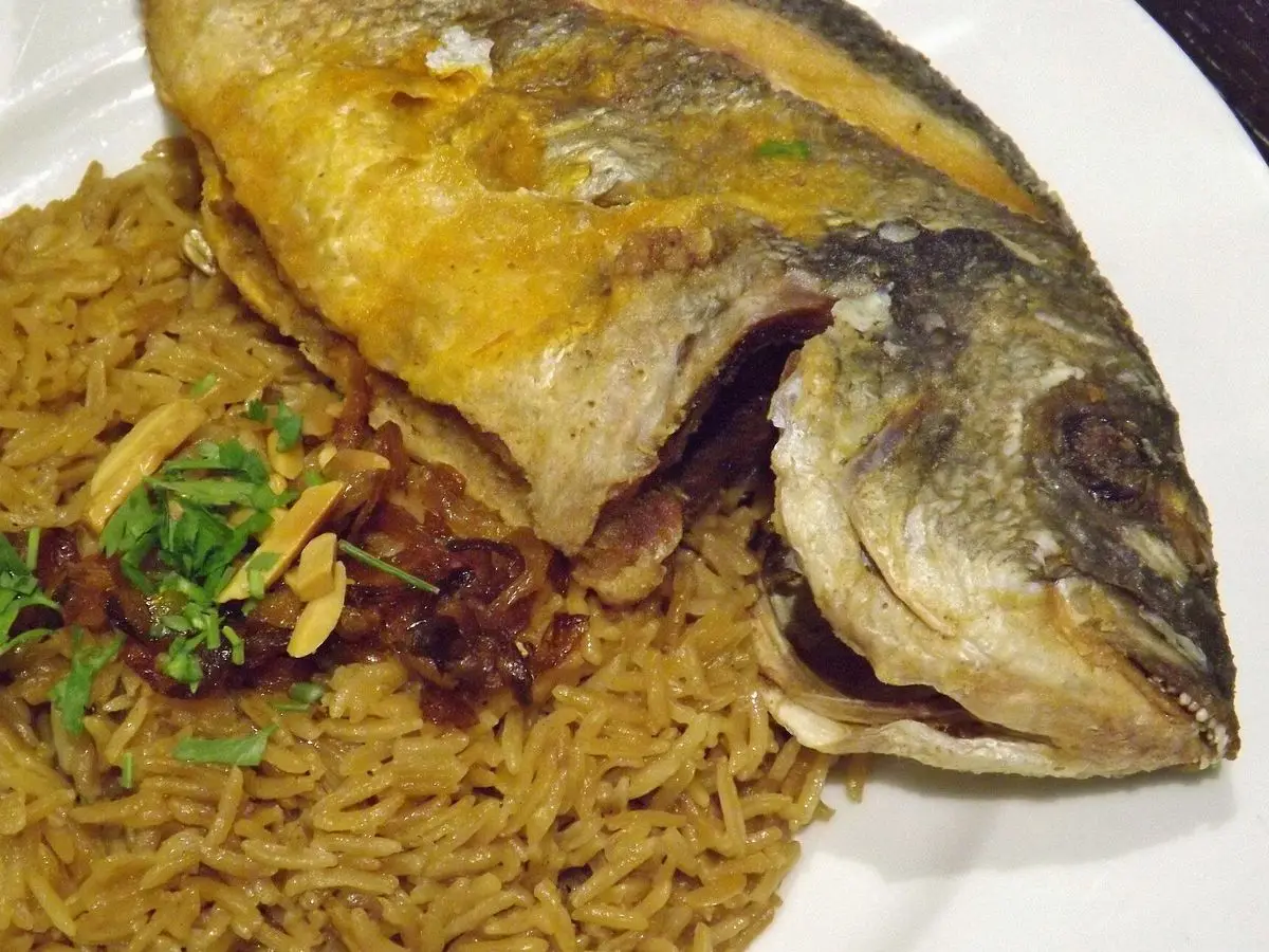 Pescado entero frito sobre arroz especiado con cebolla dorada y almendras
