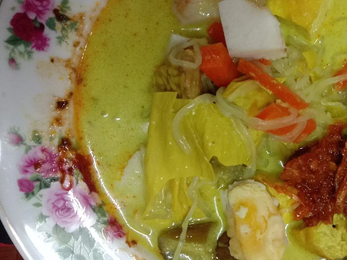 Plato de verduras cocidas en caldo amarillo de coco con zanahoria, repollo y salsa picante roja