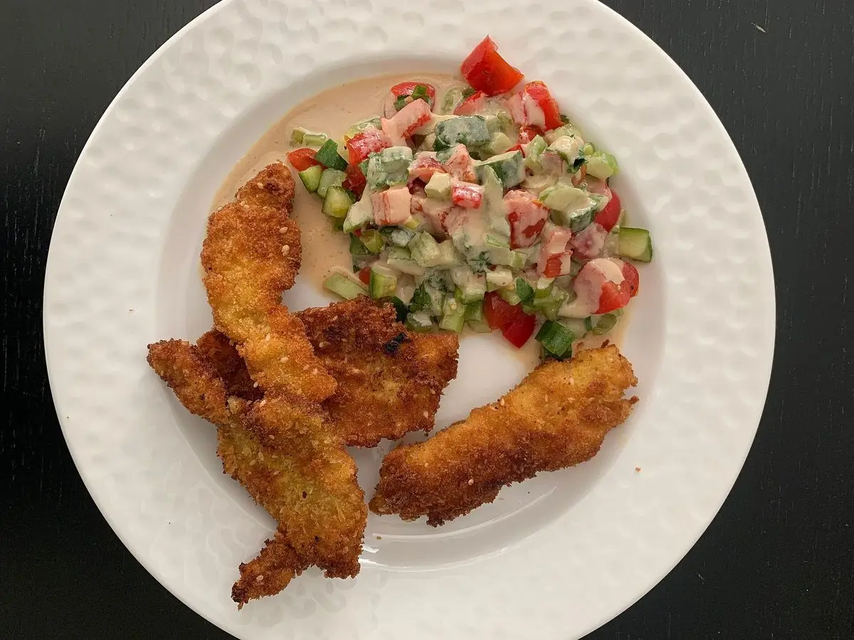 Tiras de schnitzel empanado dorado con ensalada israelí de tomate, pepino y pimiento en un plato blanco