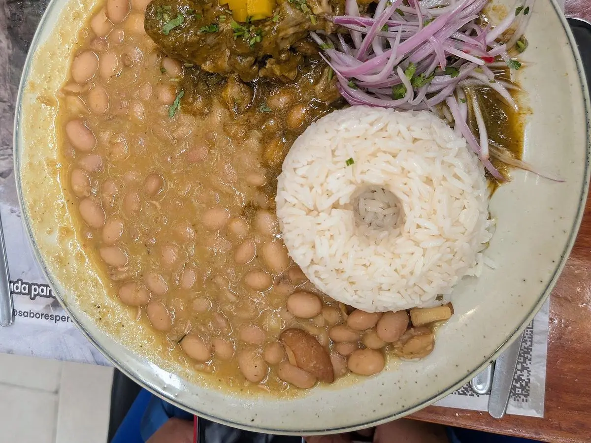 Seco de cabrito con frijoles, arroz blanco y cebolla morada en escabeche en un plato