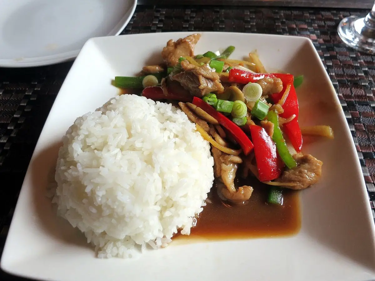 Cerdo salteado al wok con pimiento rojo y judías verdes junto a arroz blanco en un plato cuadrado
